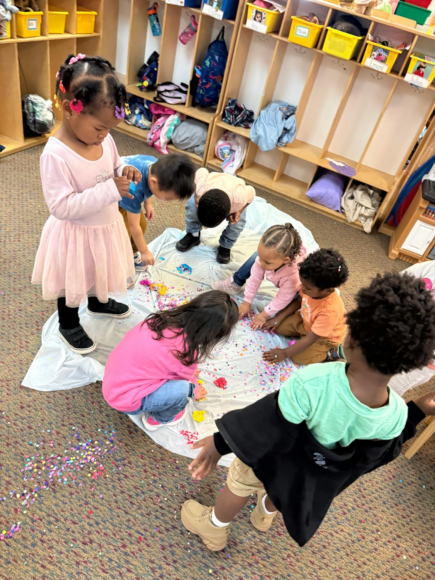 Children playing with colorful confetti on a sheet in a classroom