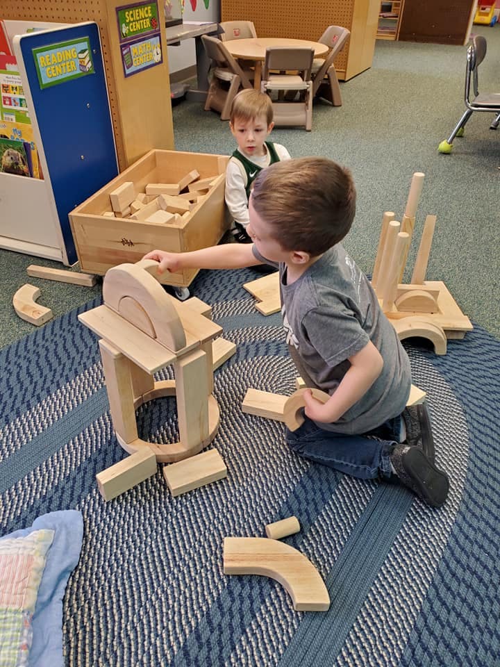 Two children playing with wooden blocks on a rug
