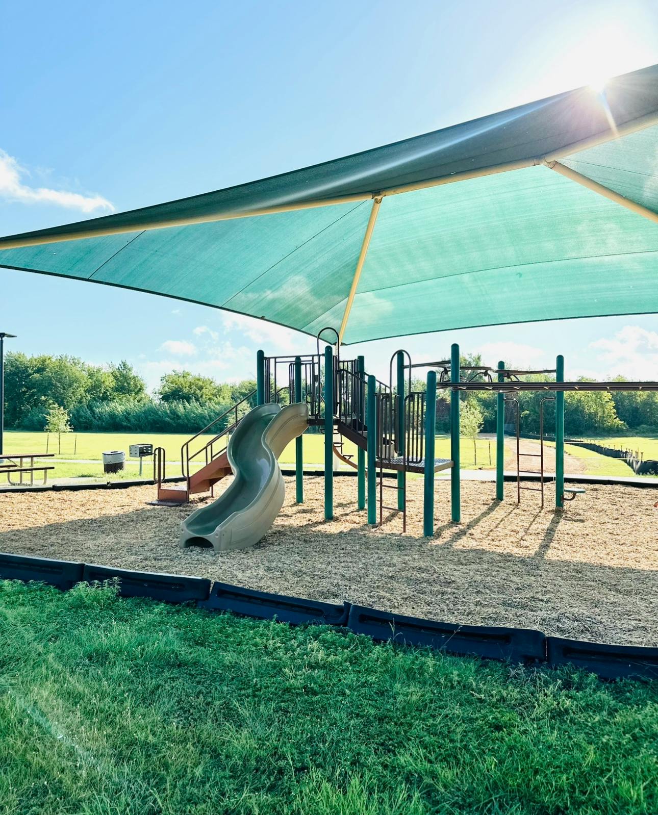 Playground with a slide and climbing structure under a large shade canopy
