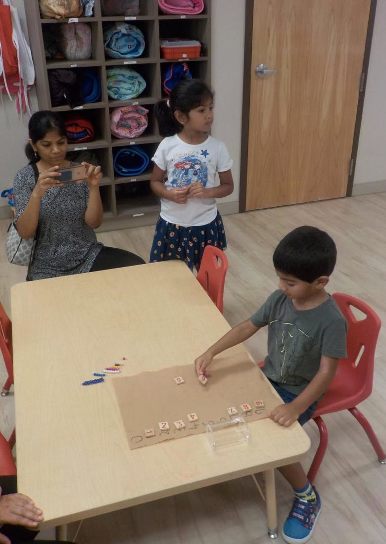 Person taking a photo of a child playing with letter tiles at a table