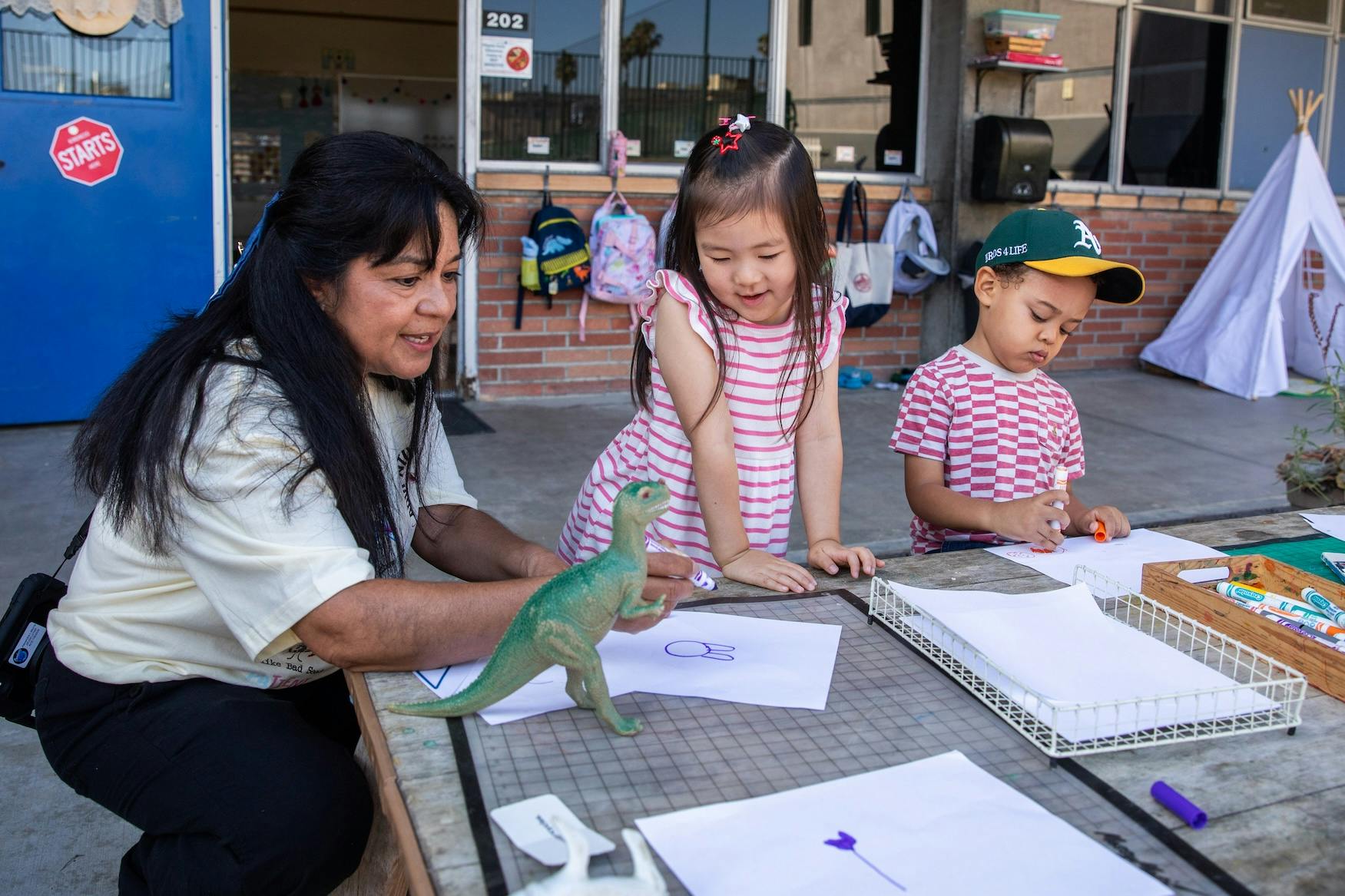 Adult and two children drawing and playing with a dinosaur toy outdoors