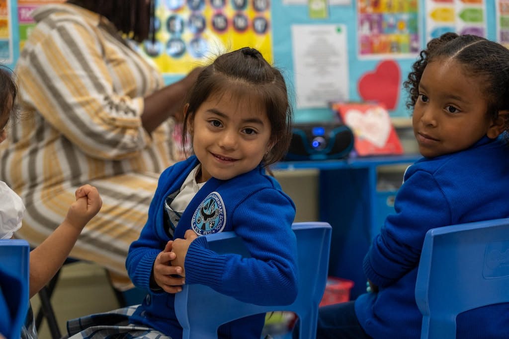 Child in blue sweater smiles while looking at camera in a classroom