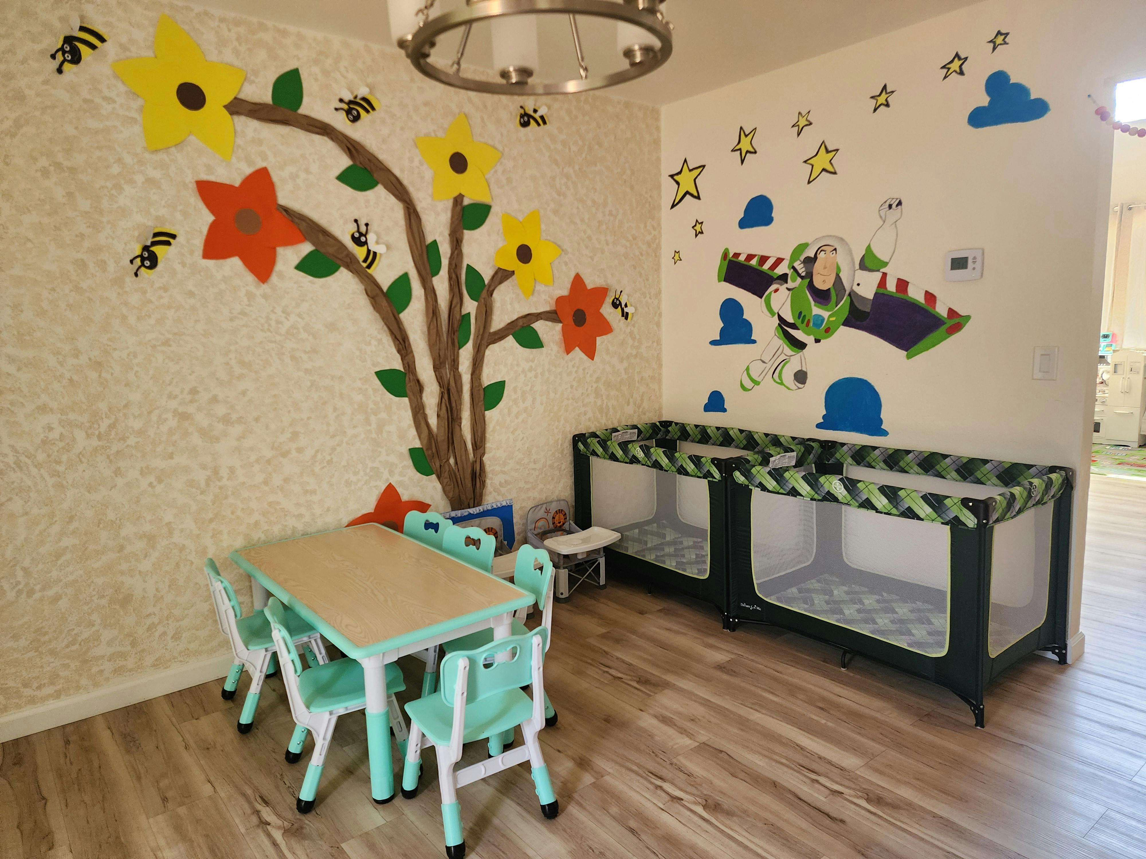 Child's room with small table and chairs, two cribs, and wall decorations