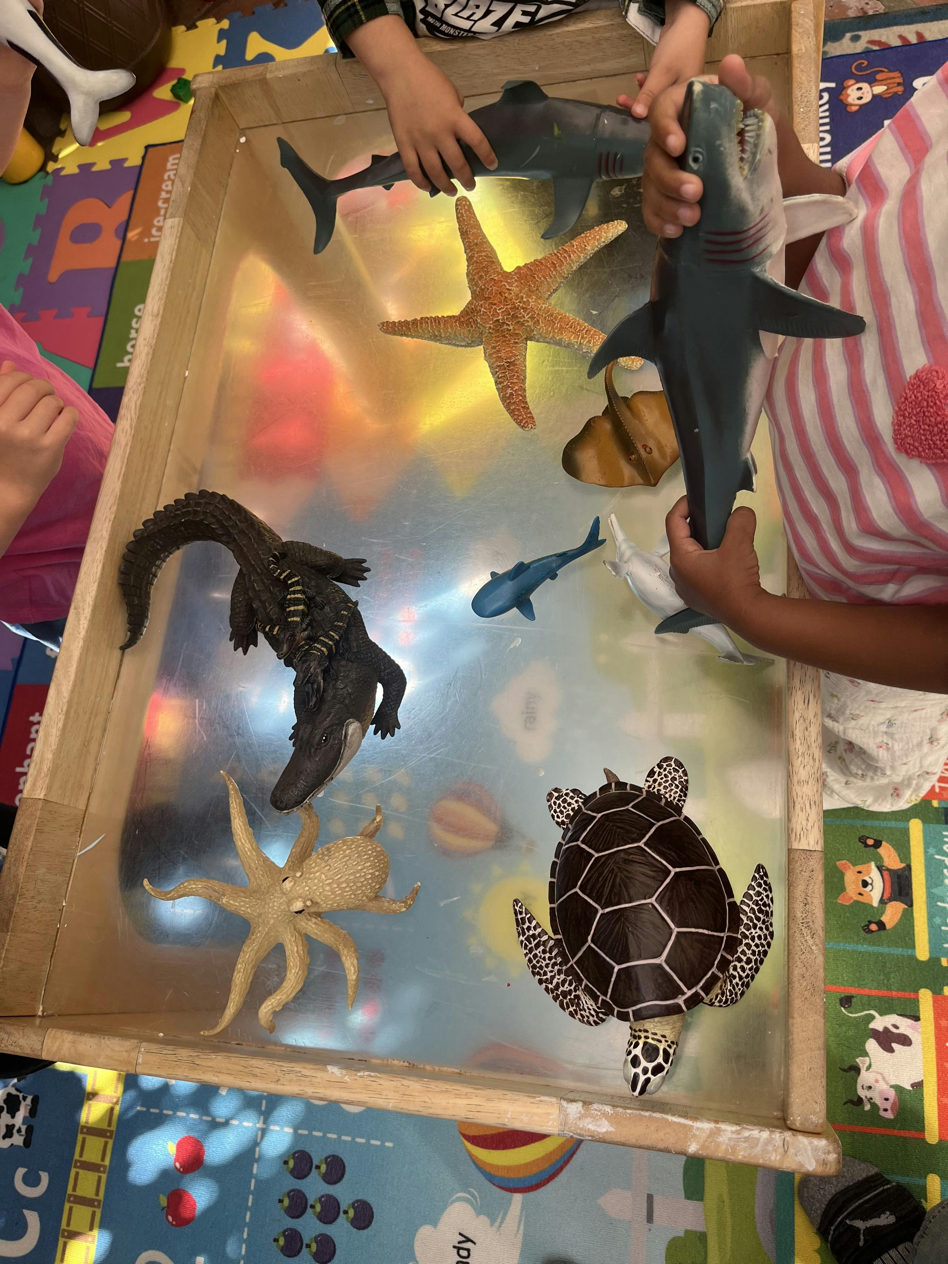Children playing with plastic sea animal toys on a light table