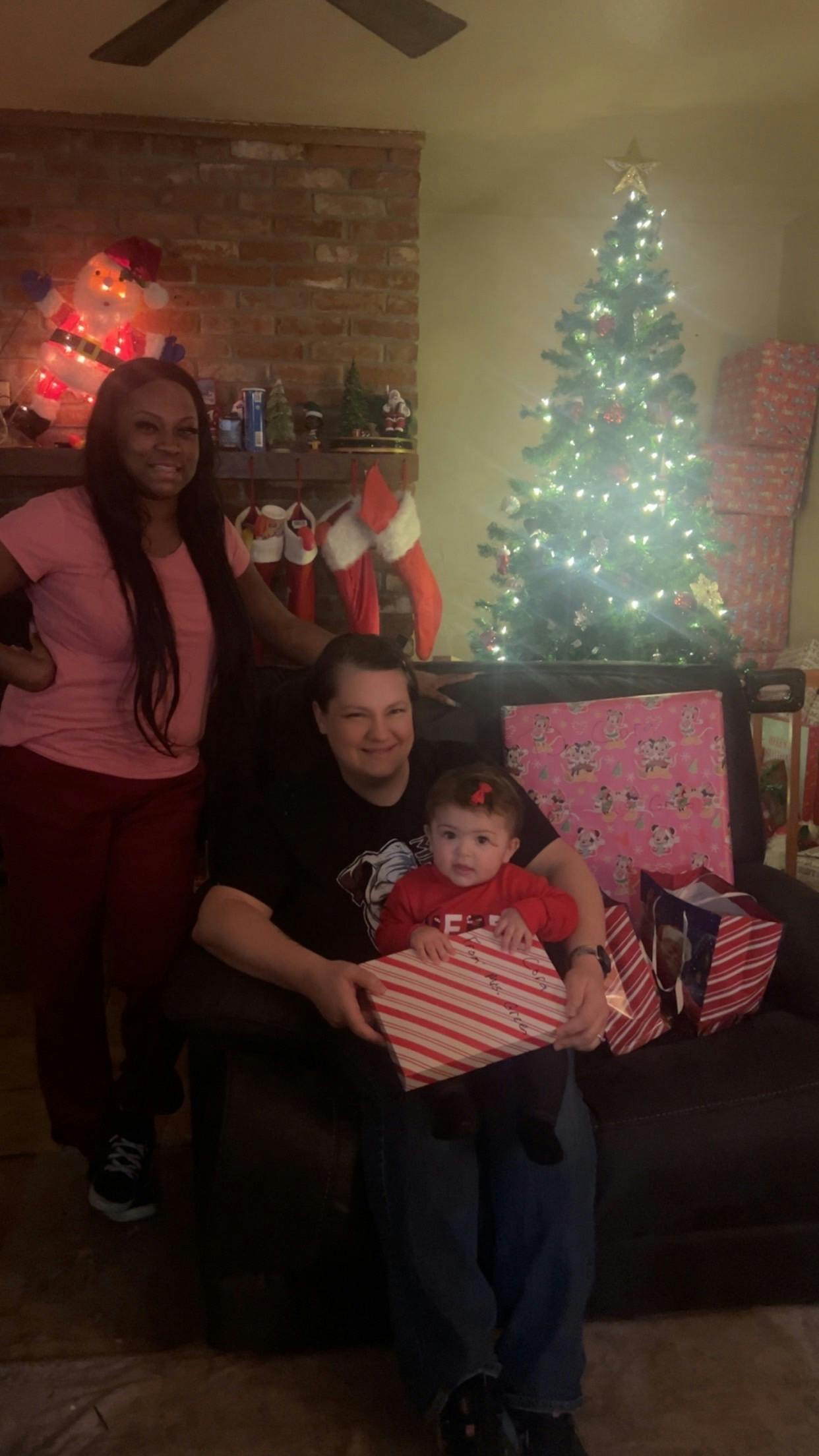 Three people with a child holding a gift in front of a Christmas tree