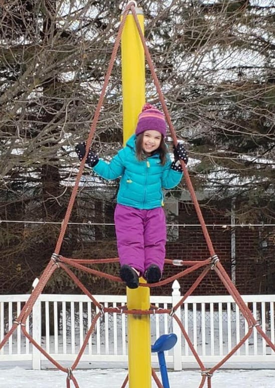 Child standing on a yellow pole in a climbing net