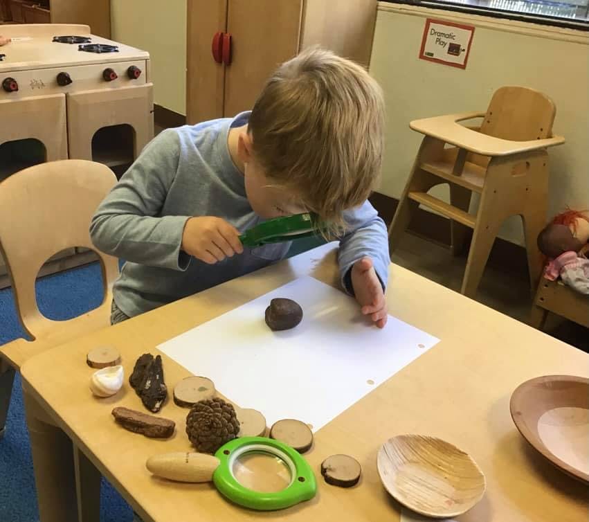 Child looking at an object through a magnifying glass at a table