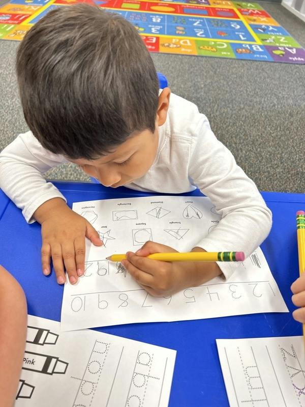 Child writing numbers on a worksheet with a pencil