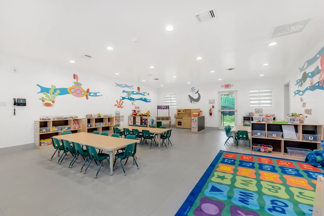 Classroom with tables, chairs, bookshelves, and a colorful rug