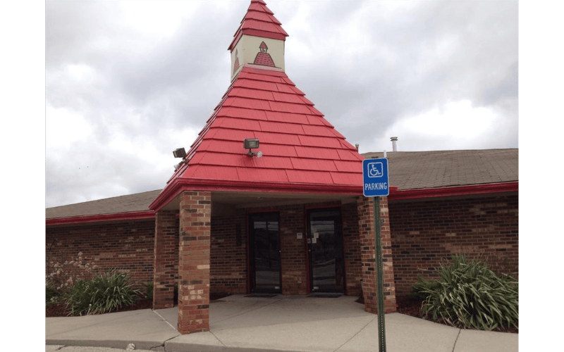Brick building with a red roof and red steeple over the entrance, a blue parking sign
