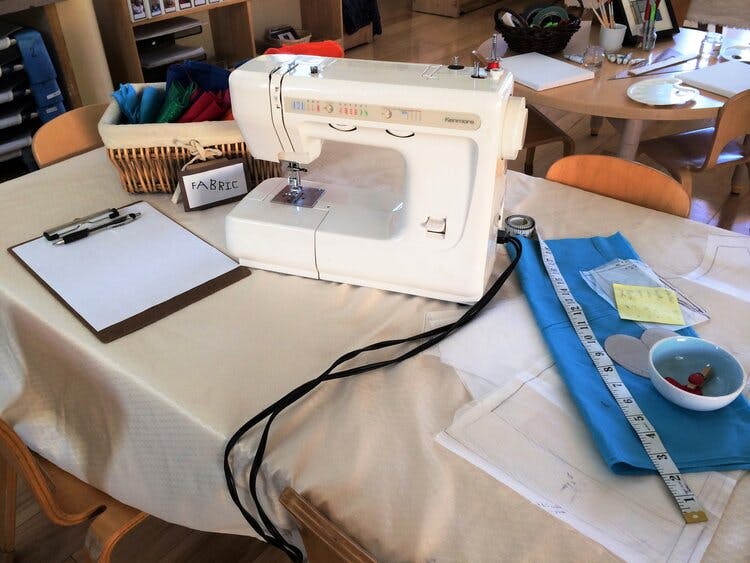 Sewing machine on a table with fabric, measuring tape, and clipboard