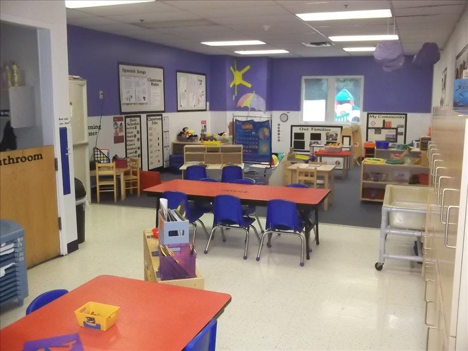 Empty classroom with small tables, chairs, and learning posters on the wall