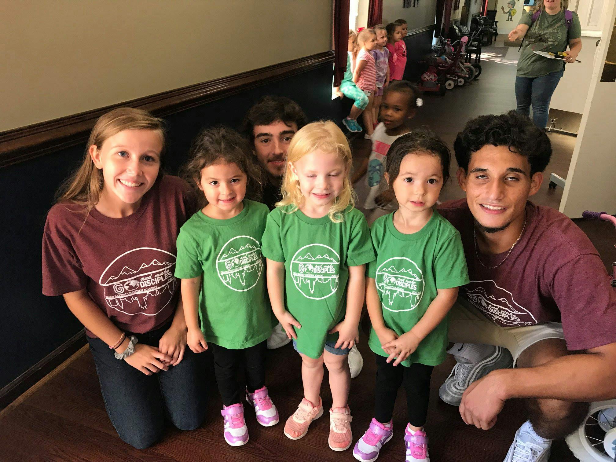 Two adults and three children in green shirts posing for a photo