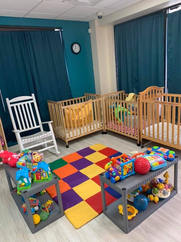 Nursery room with multiple cribs, a rocking chair, and a colorful playmat with toys