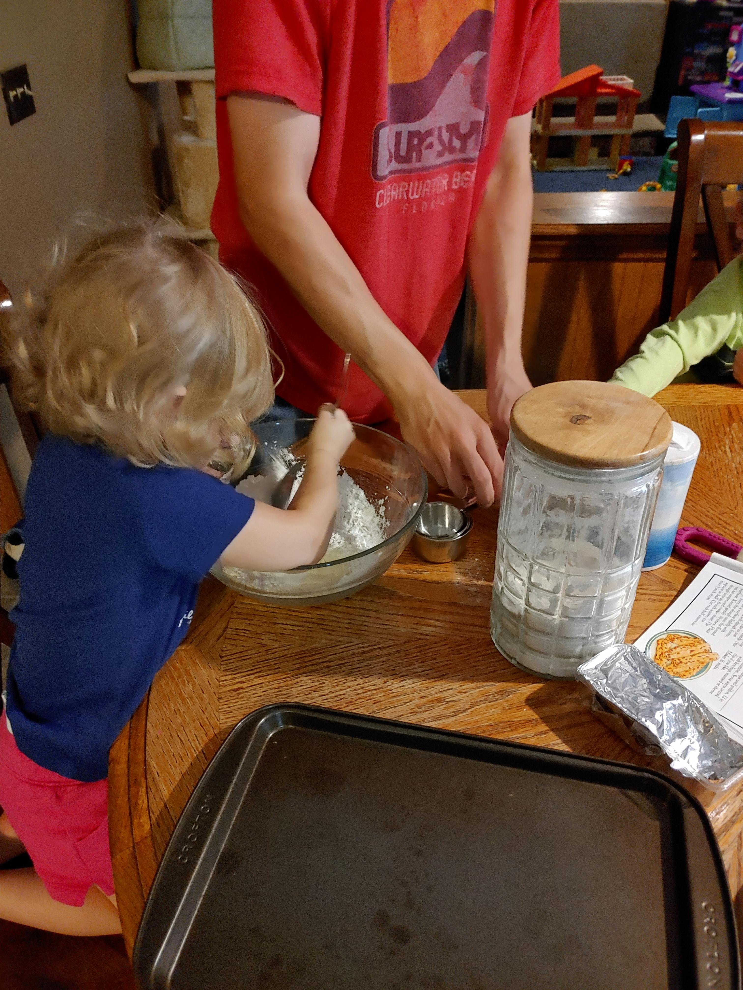 Person and child mixing ingredients in a bowl on a wooden table