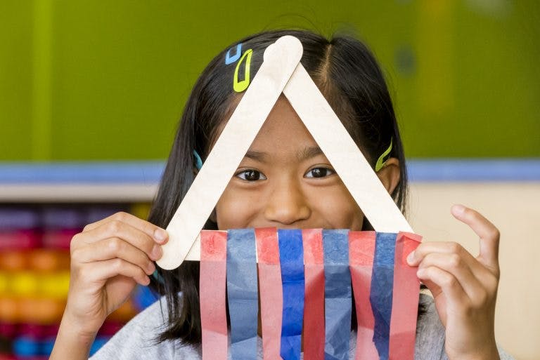 Child holding craft sticks and ribbons in front of face