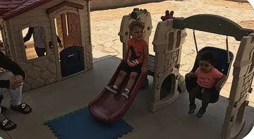 Two children on a playground slide and swing set