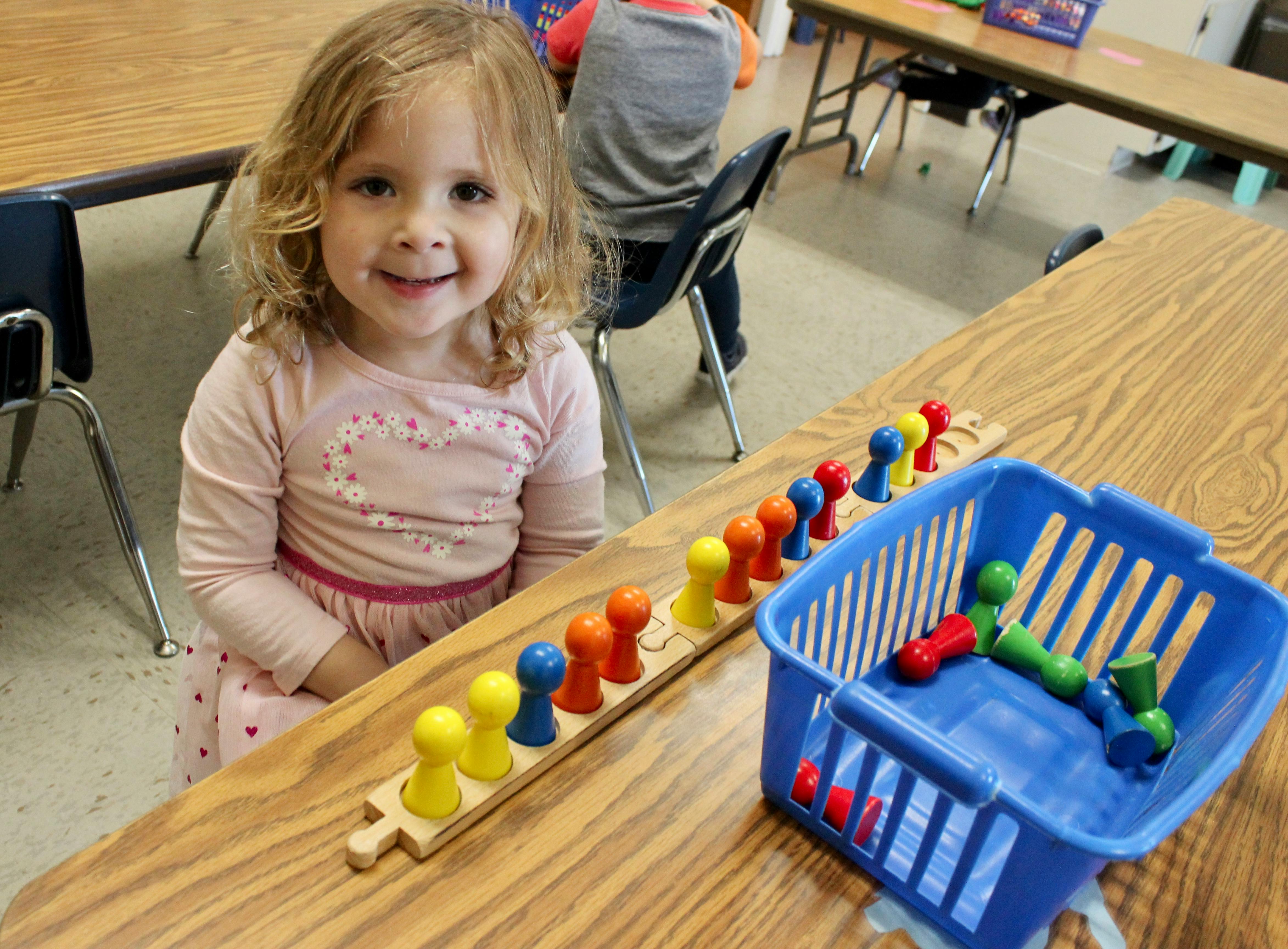 Child sitting at a table with colorful pegs and a blue basket