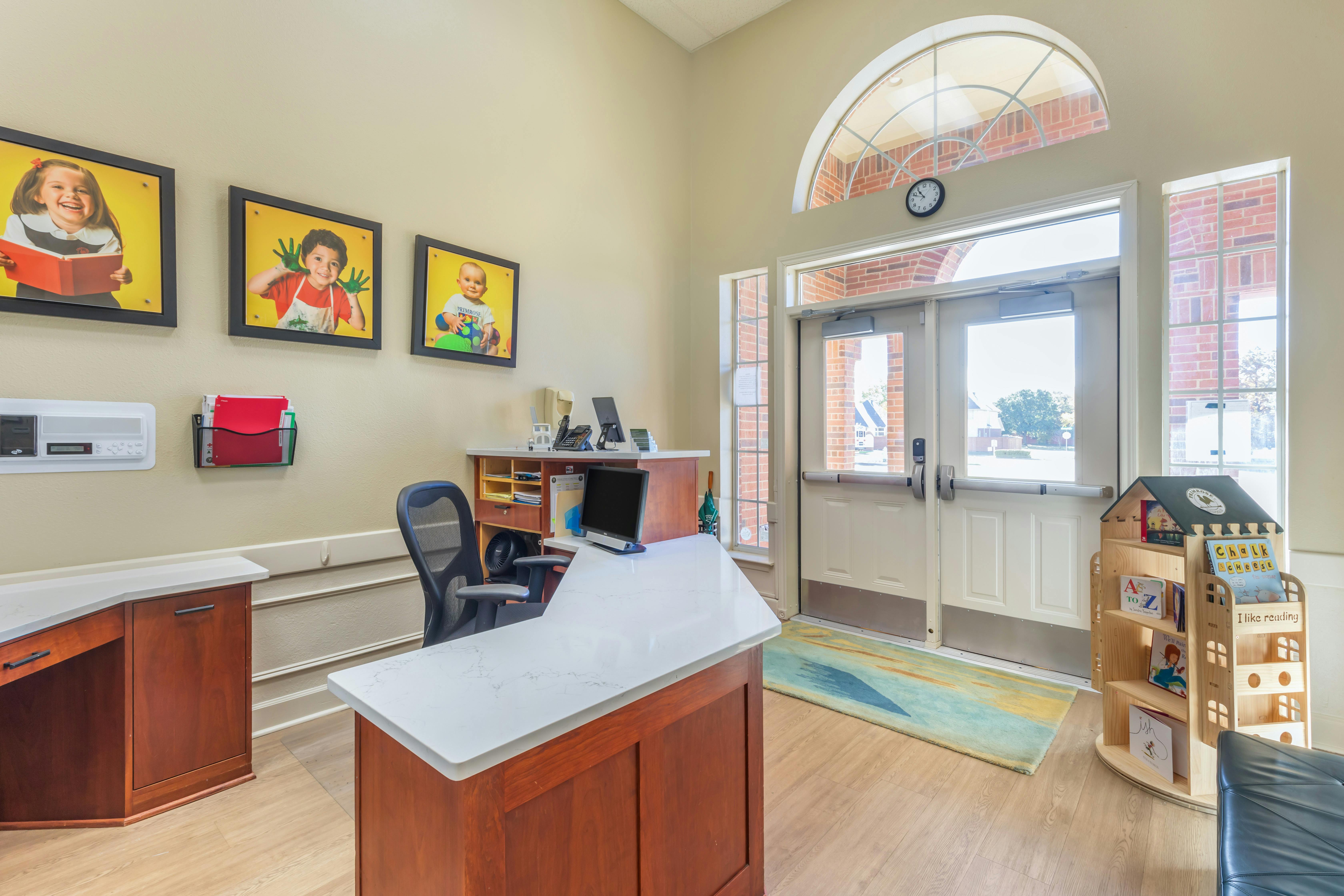 Reception area with a desk, office chair, computers, and colorful framed photos of children