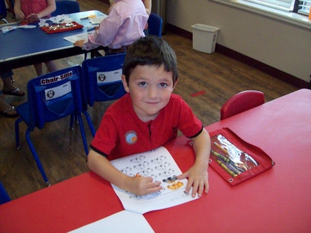 Child at a red table working on a paper in a classroom