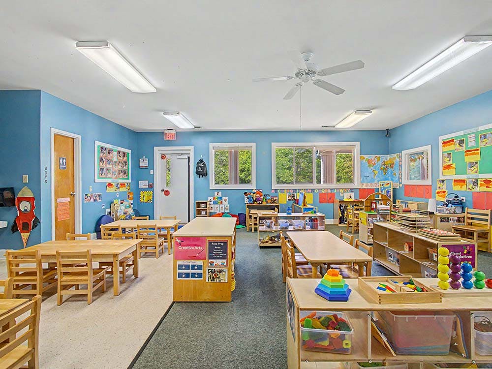 Classroom with small wooden tables and chairs, toys, and educational posters on the walls