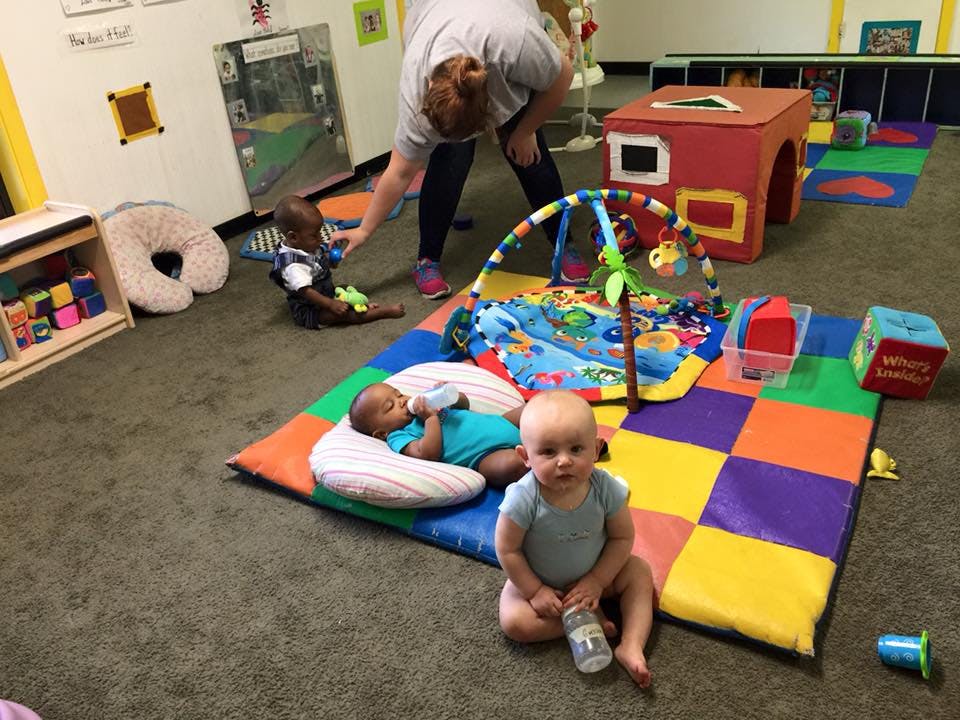 Adult interacting with children and babies on a playmat in a room