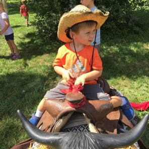 Child in a cowboy hat riding a toy bull