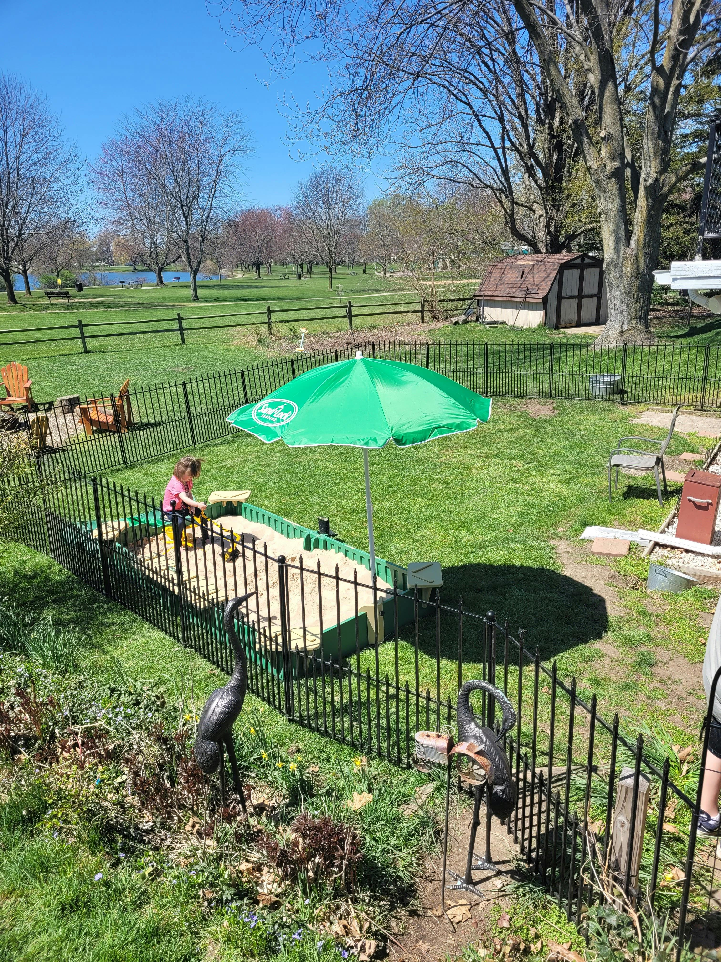 Child playing in a sandbox under a green umbrella