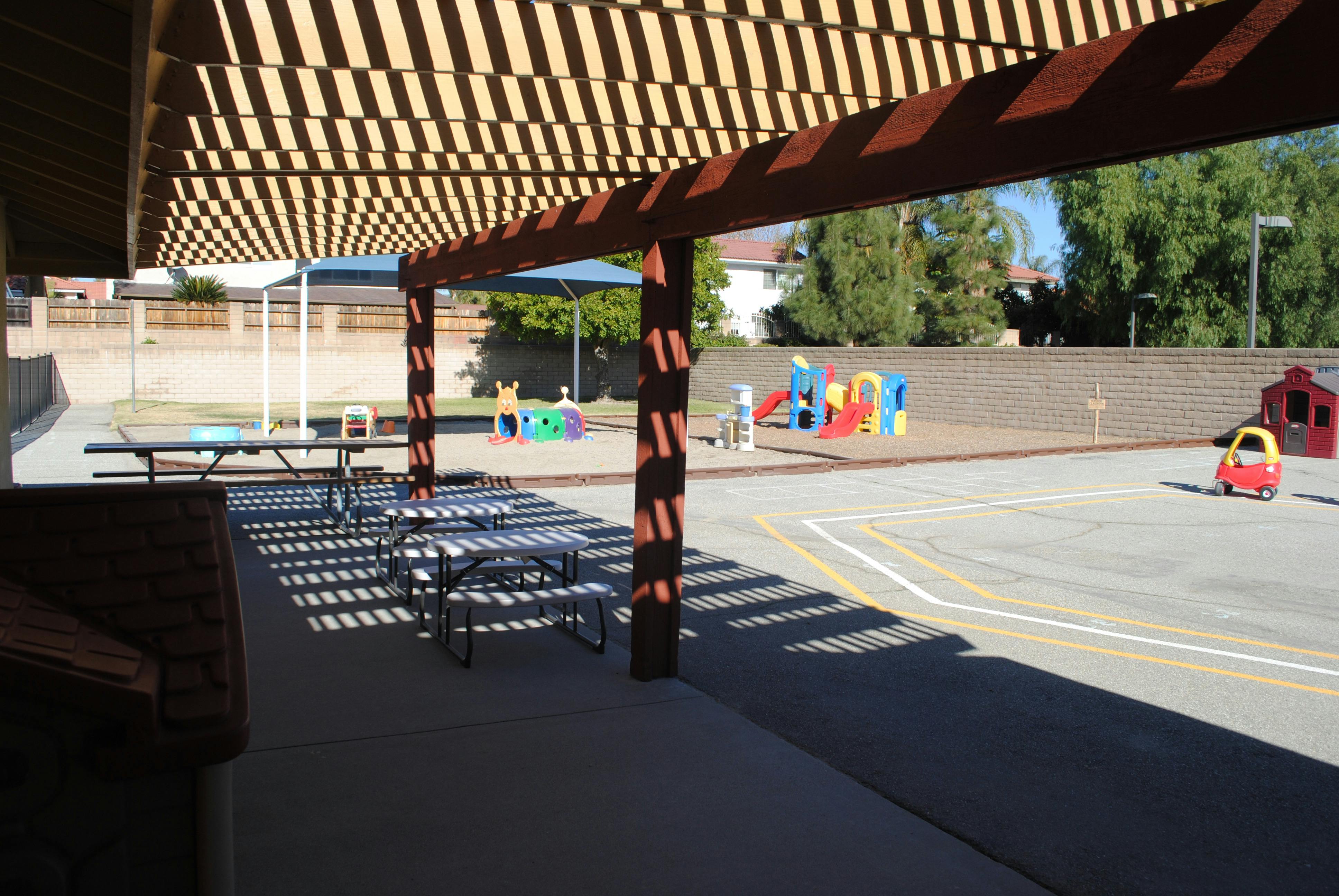 Outdoor playground with picnic tables under a shaded pergola