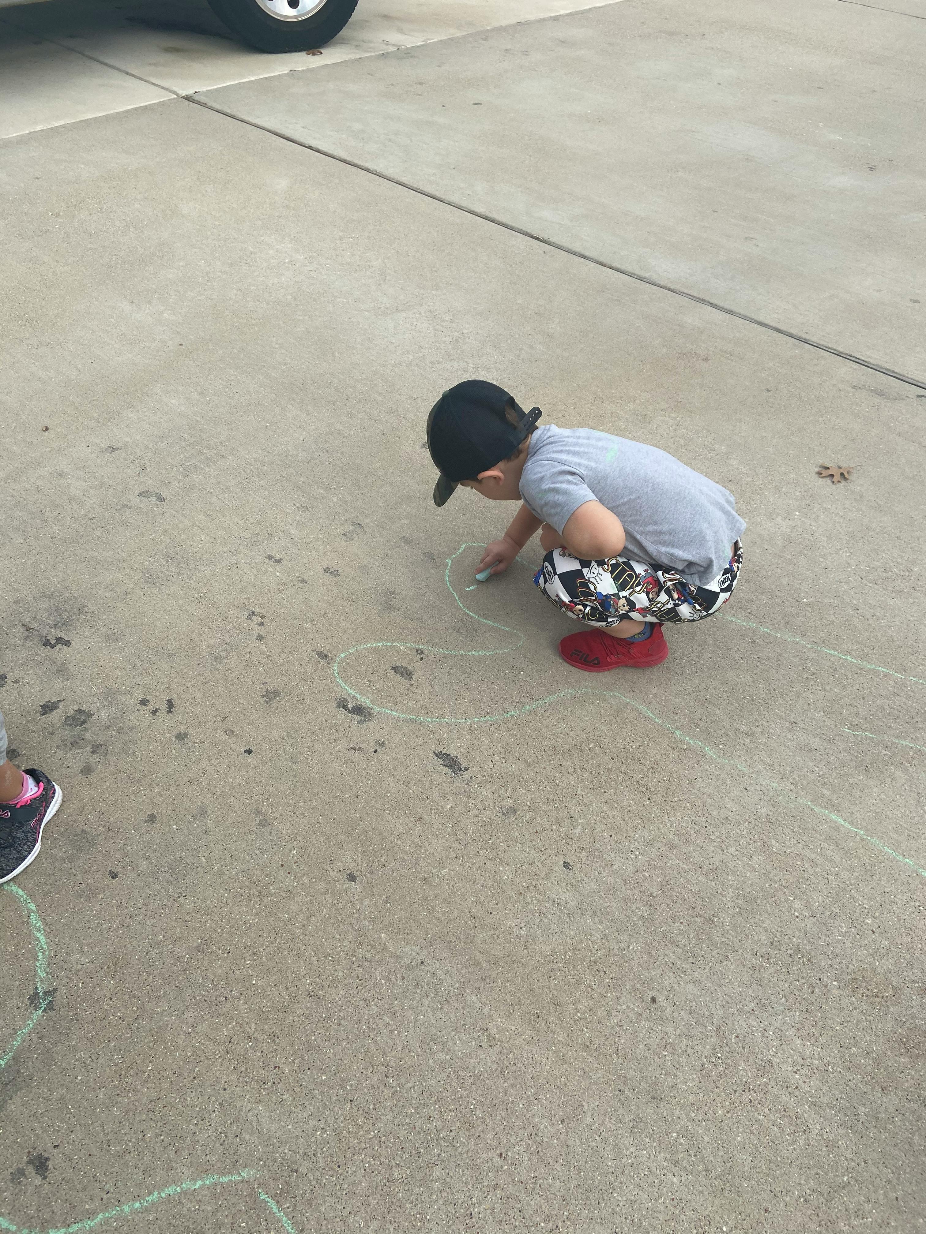 Child in a black cap drawing with chalk on concrete
