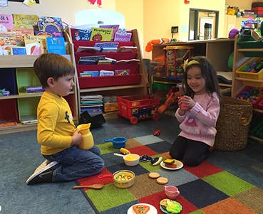 Two children playing with toy food on a colorful rug