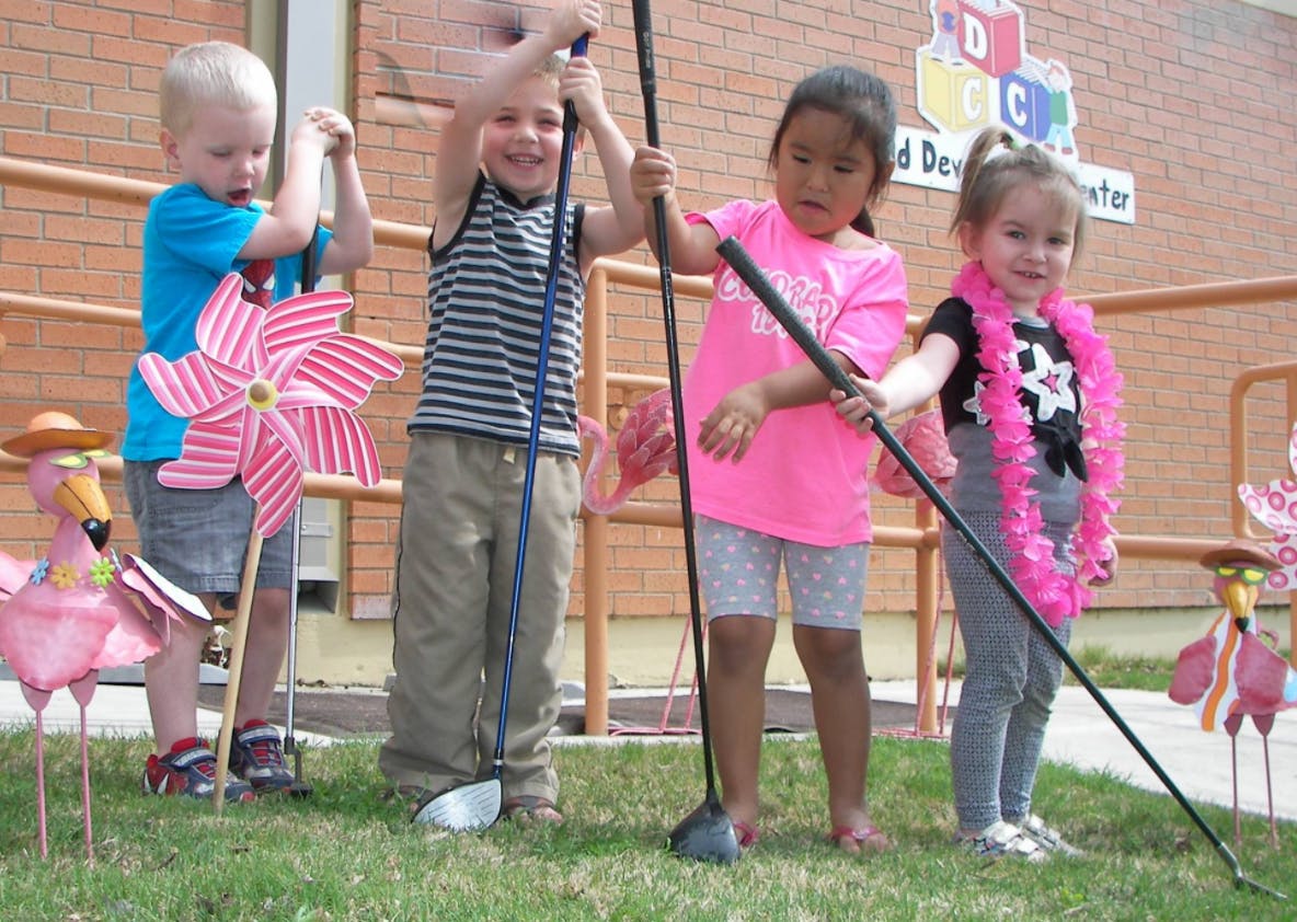Four children holding golf clubs on grass