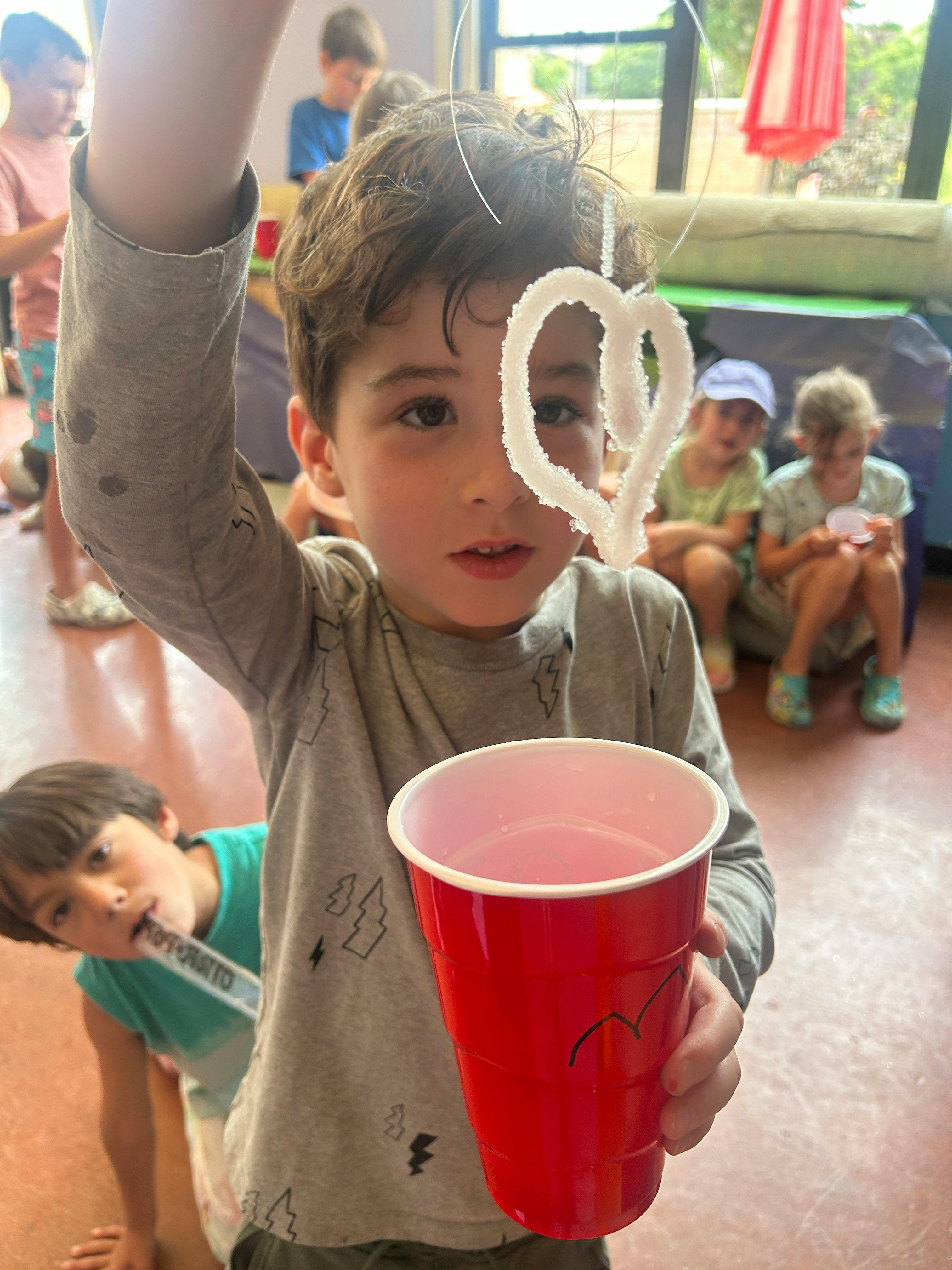 Child holding a red cup and a heart-shaped object on a string