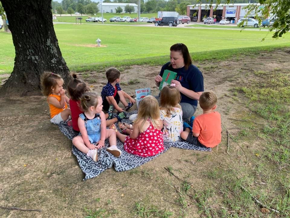 Person reading a book to a group of children outdoors
