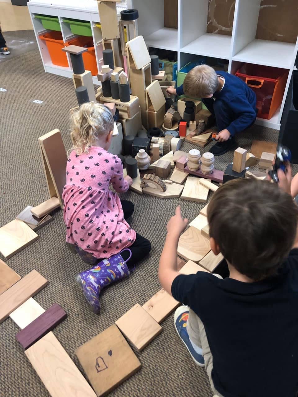 Three children playing with wooden blocks on the floor