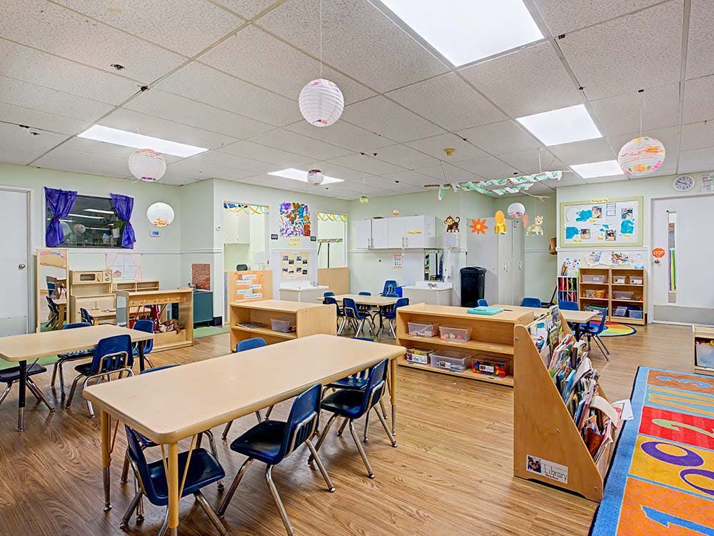Empty classroom with small tables, chairs, and shelves