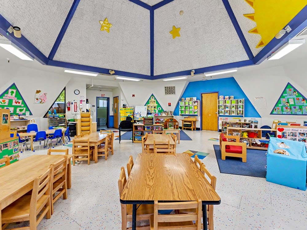 Classroom with multiple wooden tables and blue chairs arranged for children