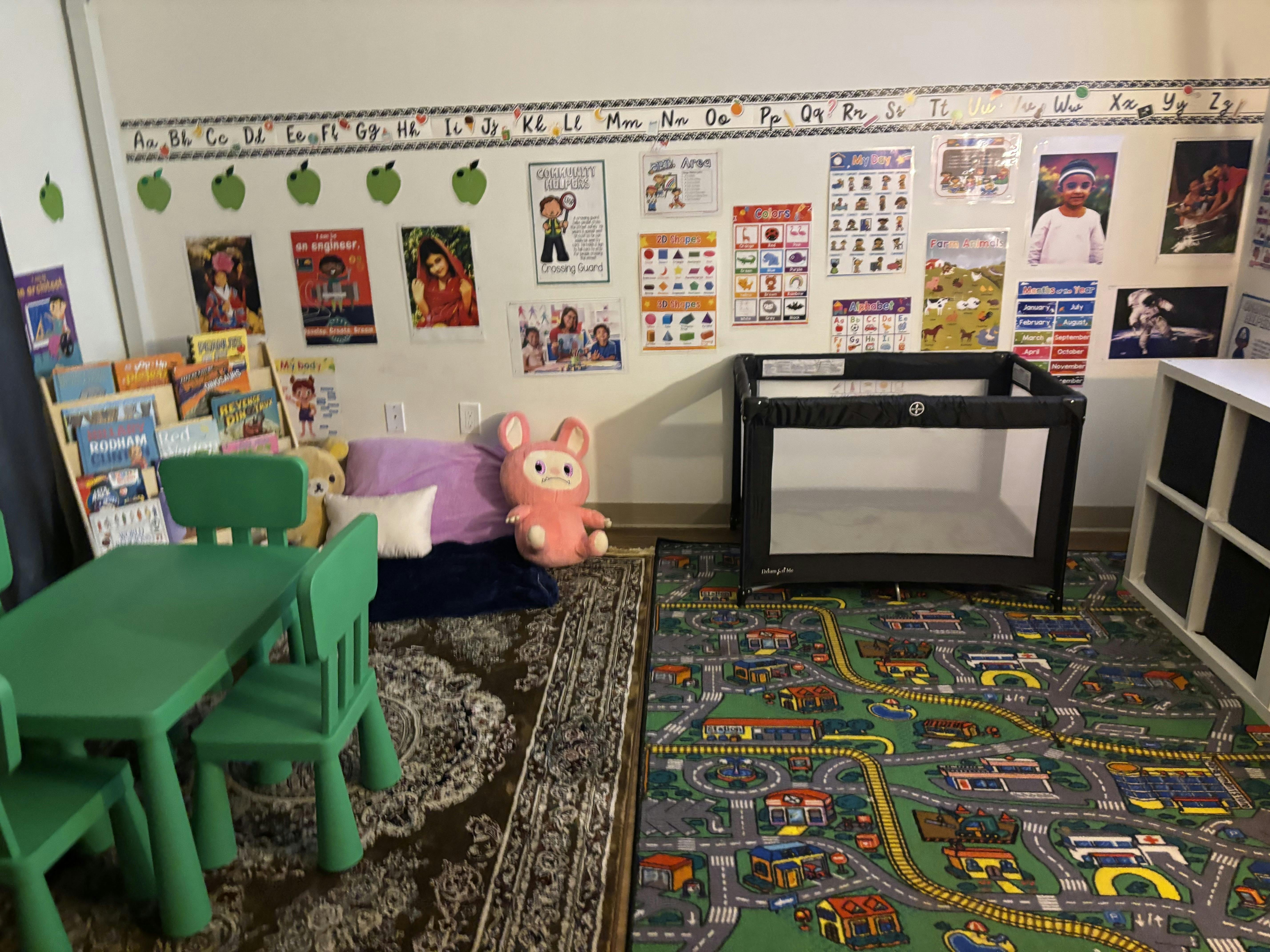 Children's play area with green table and chairs, books, and a playpen