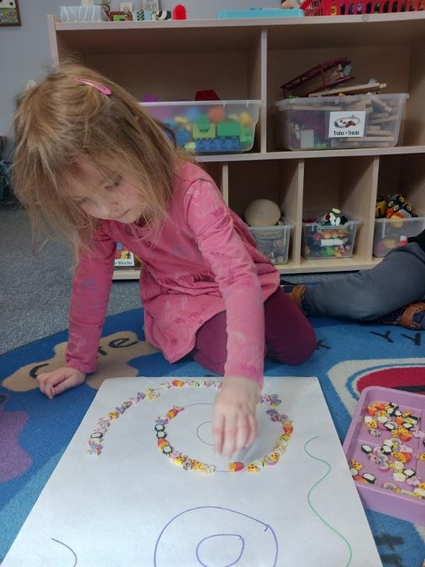 Child arranging small erasers along a drawn spiral on a large white paper