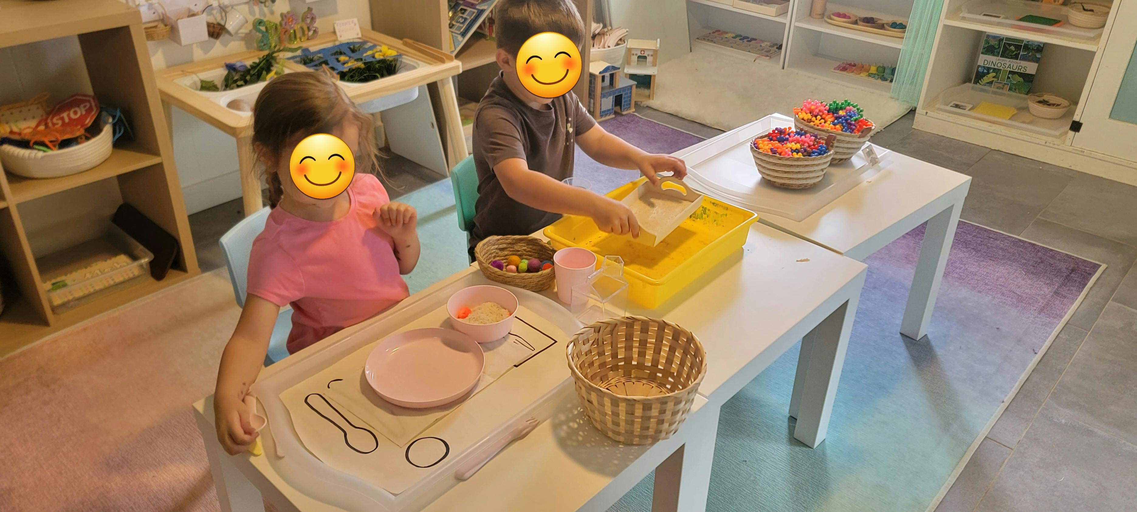 Two children at tables, one handling items in a yellow bin