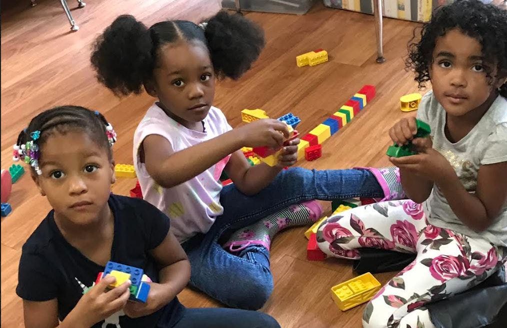 Three children sitting on a wooden floor playing with colorful building blocks