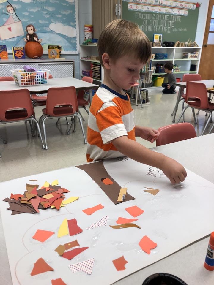 Child making a paper tree craft in a classroom