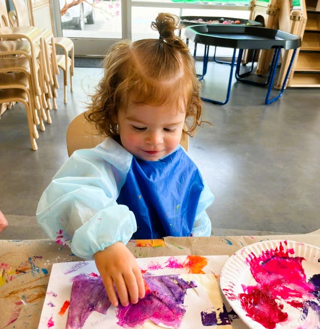 Child in smock painting with hands