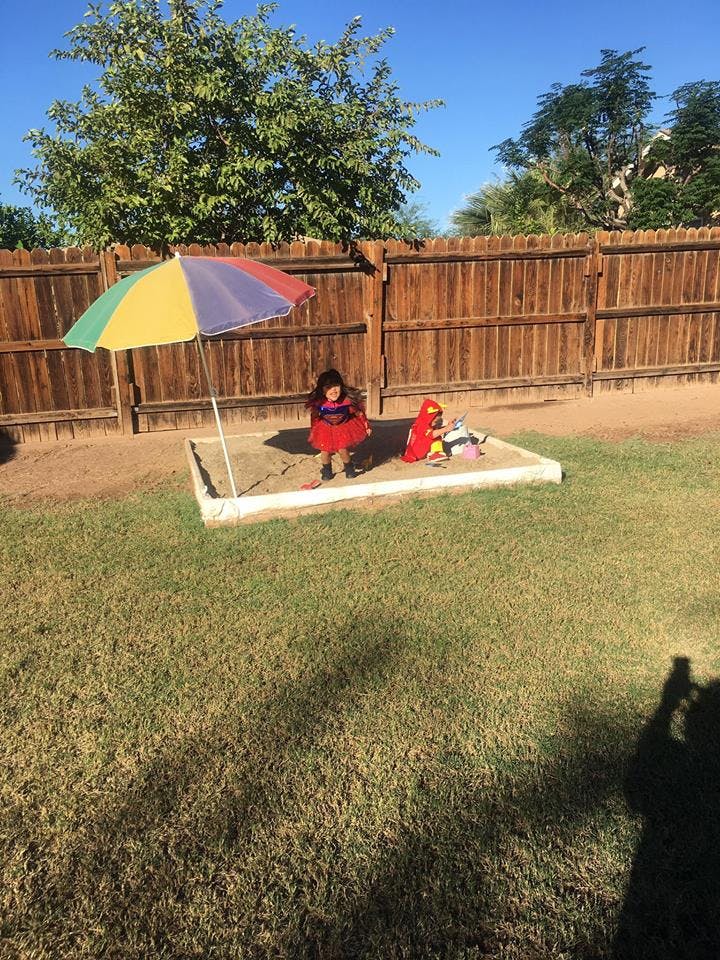 Child playing in a sandbox with a colorful umbrella