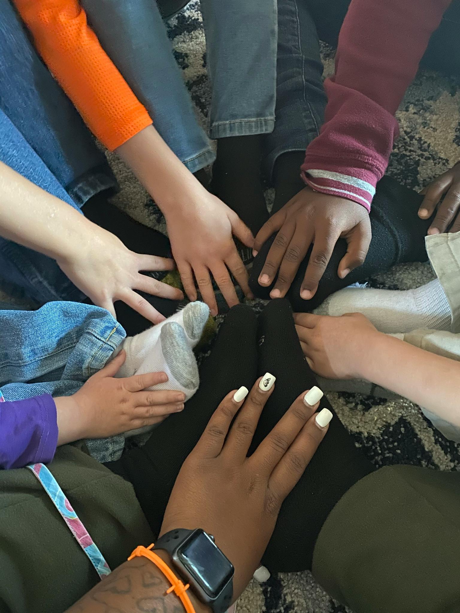 Multiple people sitting in a circle with their hands in the center