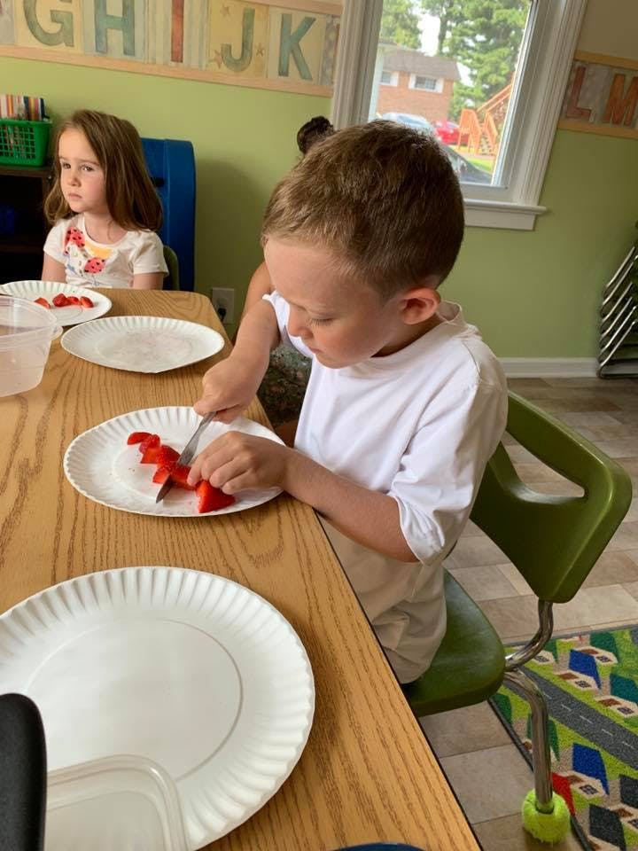 Child cutting strawberries on a paper plate at a table