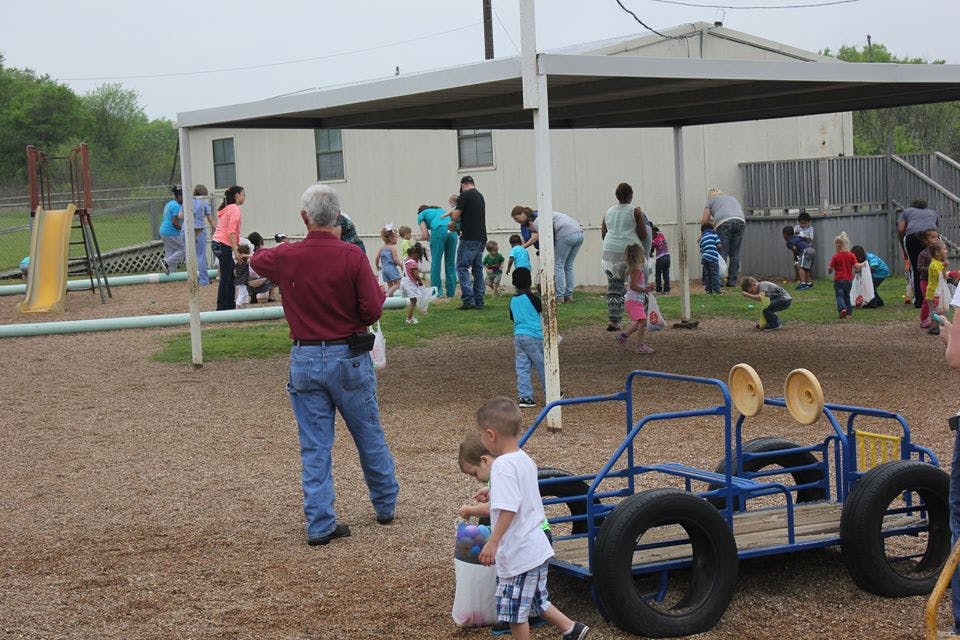 People and children on a playground with a building in the background