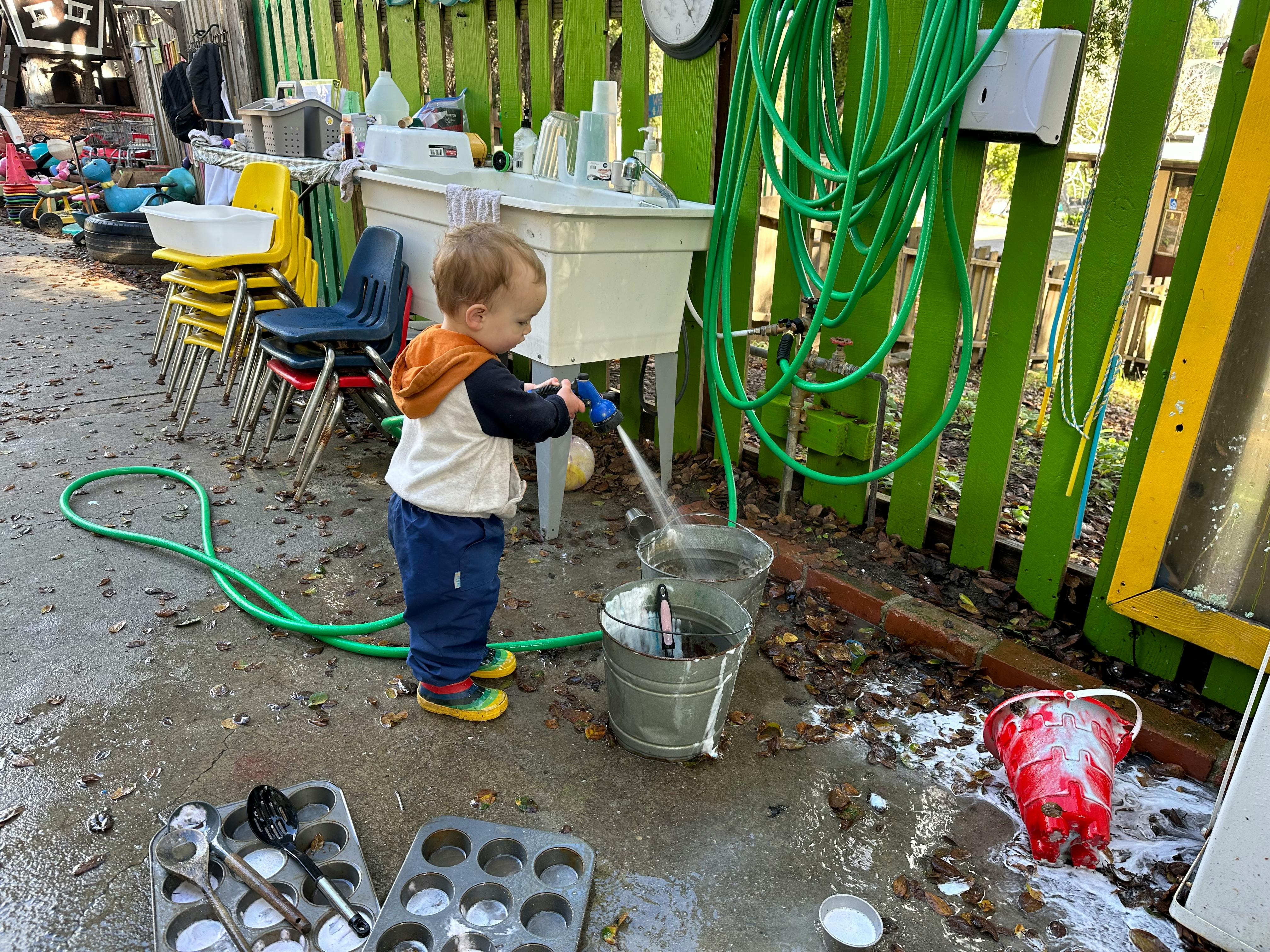 Child spraying water from a hose into buckets outdoors