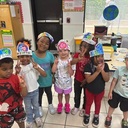 Group of children wearing Earth Day paper crowns in a classroom