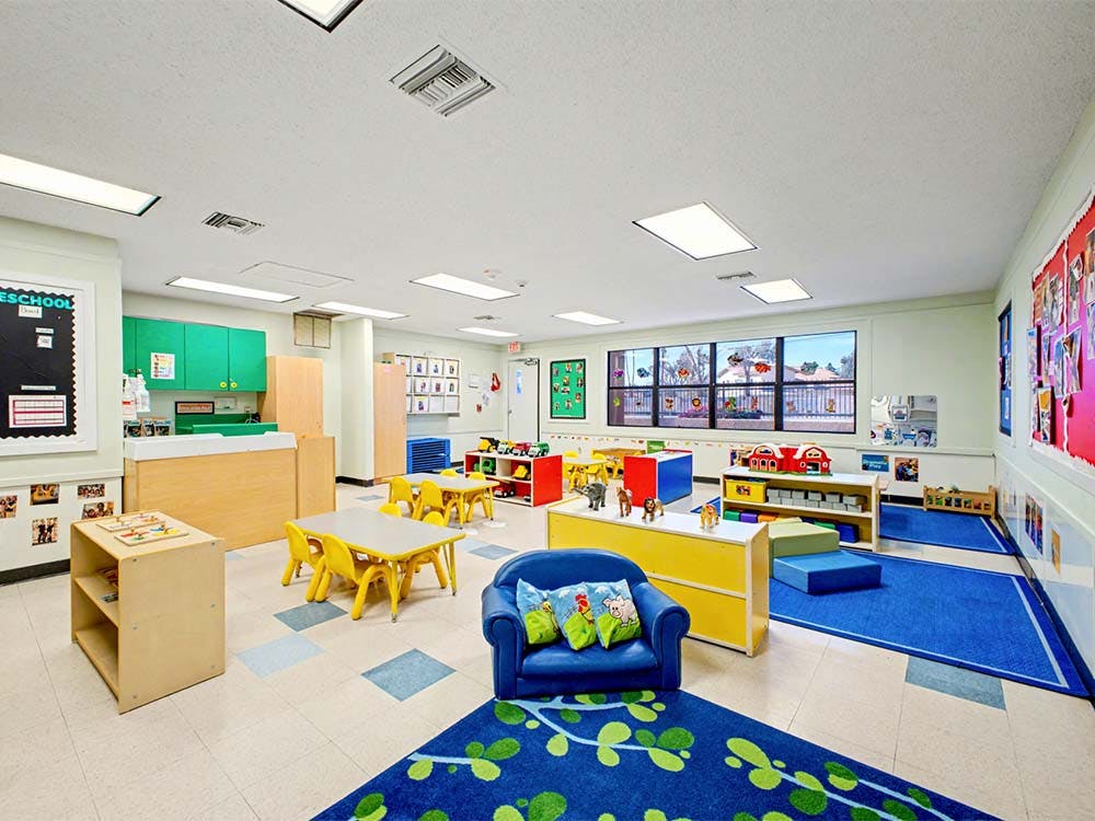 Classroom with small tables and chairs, play mats, and toys
